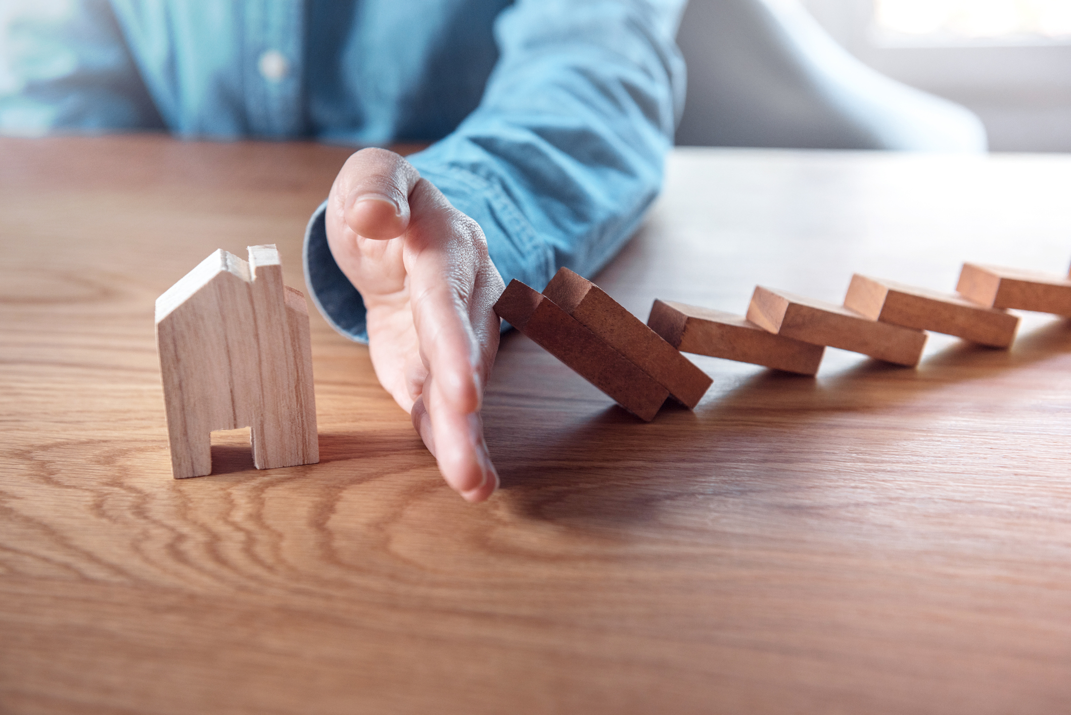 Hand stopping wooden dominoes from knocking over wooden house