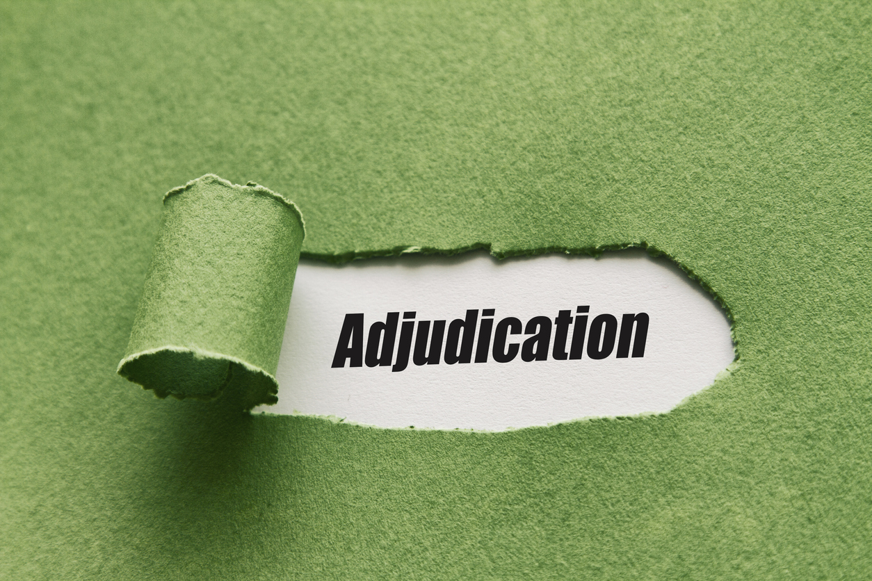 Green paper torn away to reveal the word 'adjudication'